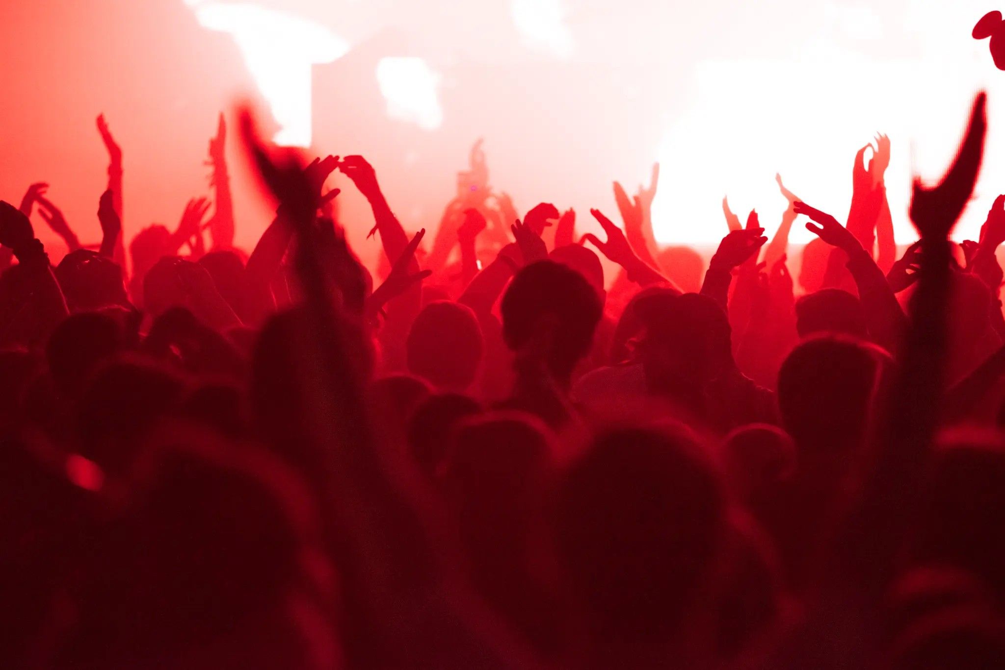 Crowd with hands raised under red stage lights at a live concert
