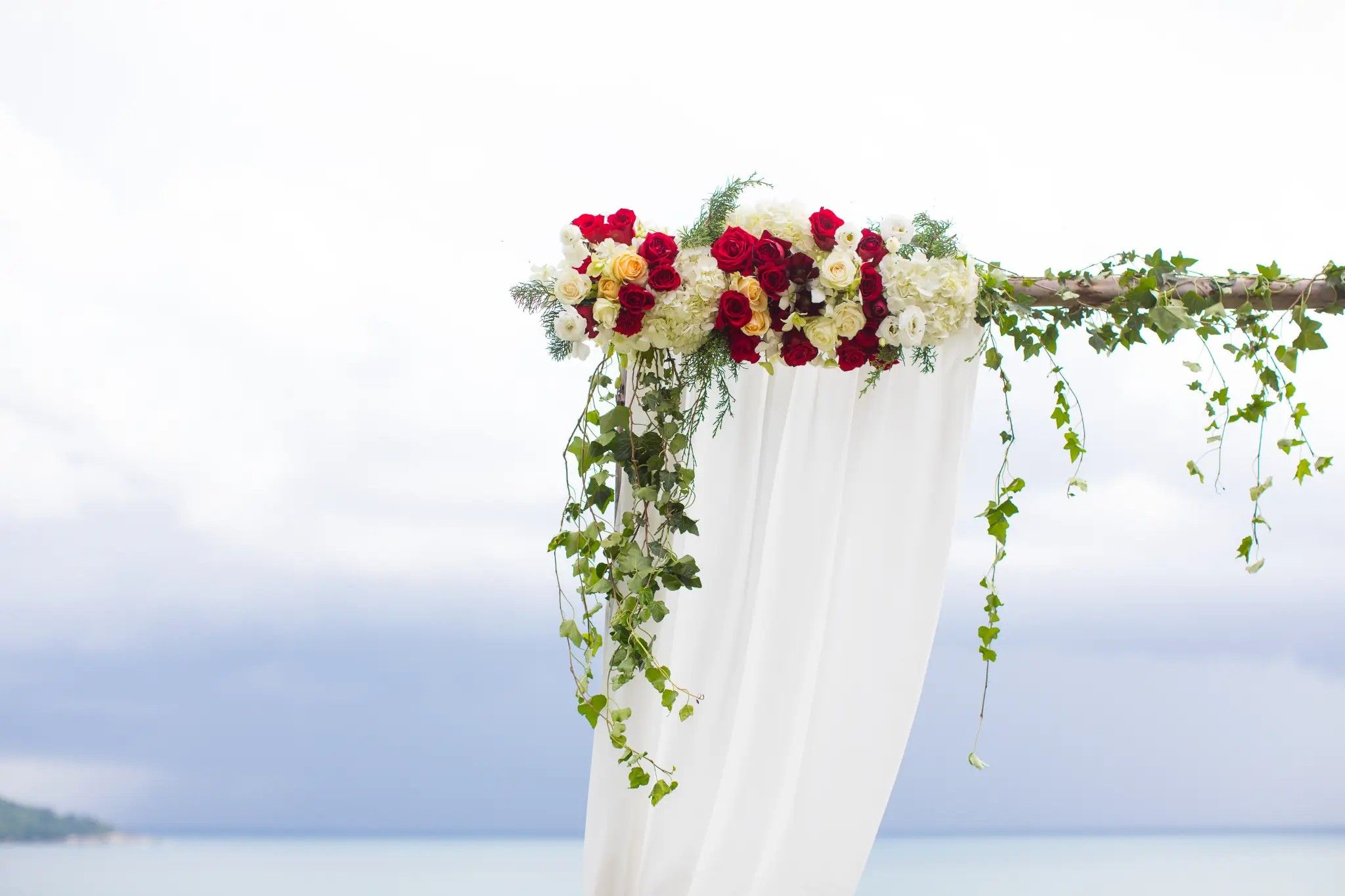 Outdoor wedding arch with red and white roses and draped fabric