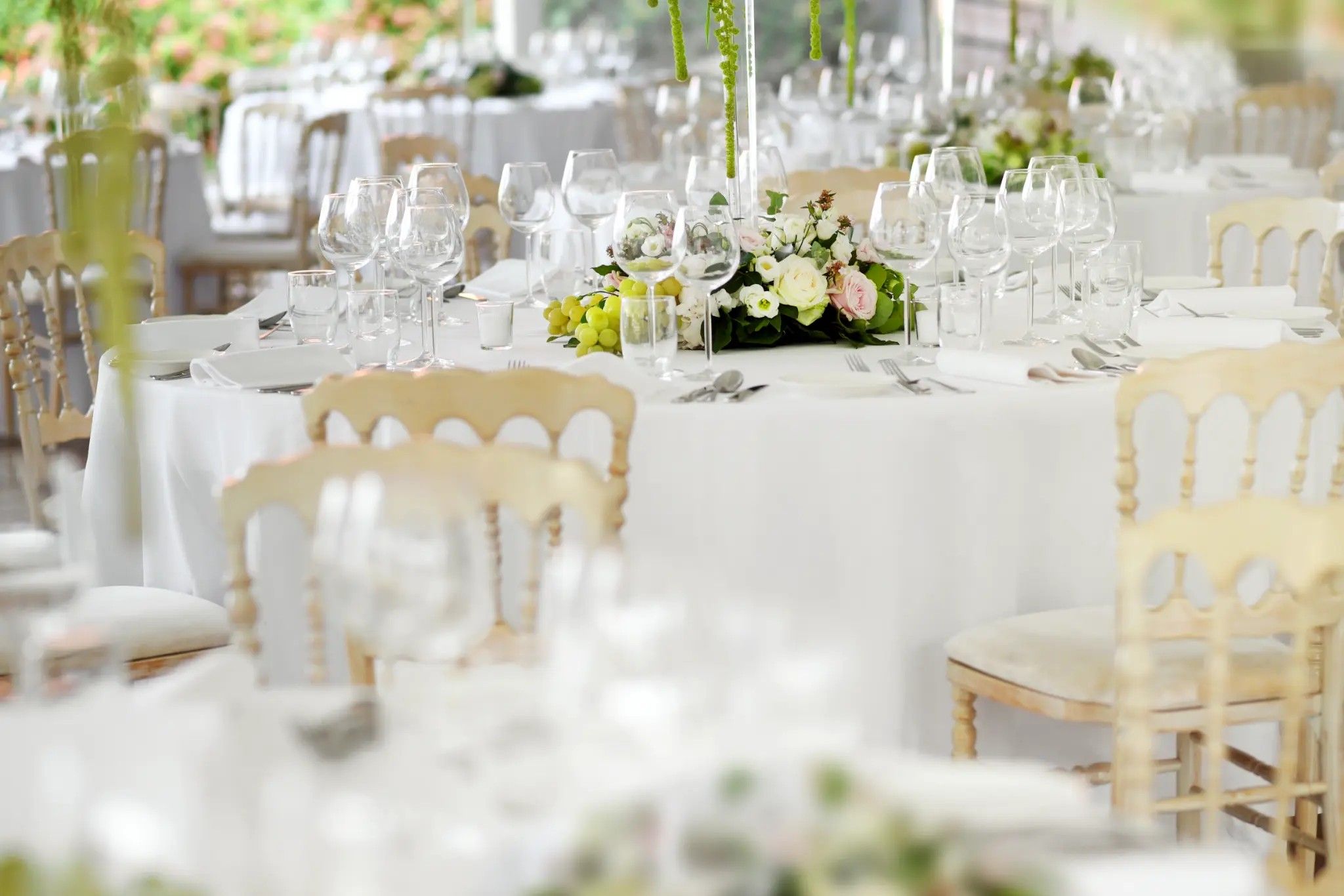 Wedding reception tables set with white florals, glassware and gold chairs
